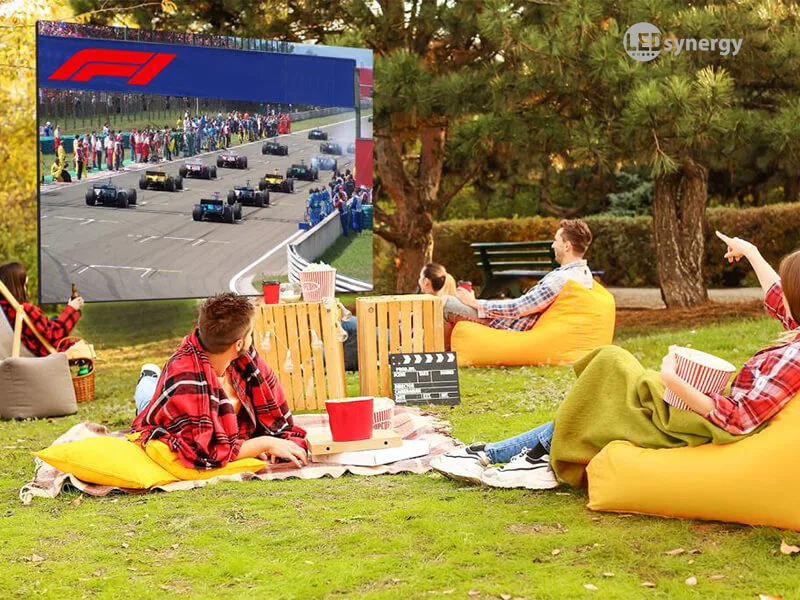 people sitting in yellow bean bags watching F1 on a large outdoor screen
